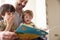 Close Up Of Father And Sons Reading Story At Home Together