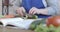 Close-up of female Caucasian senior hand cutting organic cucumber. Unrecognizable middle-aged woman preparing fresh