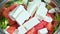 Close up of female chef hand putting Feta cheese cubes on greek vegan tomato salad with olives and lettuce leaves. The