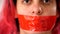 Close-up female face. Red tape sealed mouth. Serious woman with her lips covered by a tape