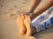 Close up of female feet. Woman sitting on the sand, practicing yoga. Paschimottanasana, Seated Forward Bend Pose. Hands holding