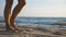 Close up of female foot stepping on the sand with sea waves at background. Beautiful woman walking on the coast barefoot