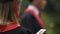 Close-up of female graduate in academic gown reading message on smartphone