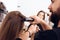 Close up. Female hairdresser straighten brown hair to woman using hair iron in beauty salon.