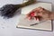 Close-up of female hand with beautiful manicure holding golden pink brilliant pen on the checkered notebook with bouquet of lavend