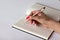 Close-up of female hand with beautiful manicure holding golden pink brilliant pen on the checkered notebook on the light backgroun