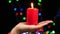 Close-up of female hand with a big red candle on bokeh background. Burning candle on a black background. Religion