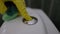 Close-up female hand cleaning toilet button with sponge and detergent. Closeup unrecognizable woman in gloves