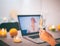 Close up of female hand with glass of champagne in front of laptop screen celebrating online video chatting