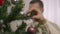 Close-up of female hand hanging New Year toy on Christmas tree with blurred man decorating at background. Unrecognizable