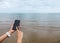 Close up of Female Hand Holding Smart Mobile Phone with Blank Screen on The Beach with Clear Sky, Beach Sand and Wave used as Temp