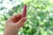 Close-up female hand holding a tube with new pink, peach lipstick on natural background of summer foliage, wants to do makeup,