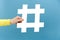 Close up of female hand holding white hashtag sign, marketing symbol, followers concept, posing isolated over blue color