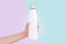 Close-up of female hand holding white reusable steel thermo water bottle isolated on two background of blue and purple colors.