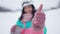 Close-up of female hand in pink mitten showing thumb up with blurred female skier at background. Unrecognizable