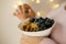 close-up female hand takes berries on blurred background with bokeh, healthy food white cup, oatmeal, blueberries, nuts, almonds,