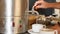 Close-up, female hand turns on the tap of hot water container, then pours boiling water into a cup with a tea bag in it