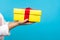 Close up of female hand in white sweater holding yellow wrapped present box, giving gift. studio shot isolated on blue background