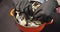 Close up of female hands in black gloves picking mussels with cream sauce from a bowl. Mediterranean food