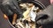 Close up of female hands in black gloves taking mussels with truffles from a bowl