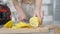Close-up female hands cutting vitamin citrus lemon with kitchen knife on cutting board. Unrecognizable slim young woman