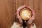 Close-up female hands holding cup with coffee cappuccino with foam with nice pattern. Perfect red gel polish manicure. Wood