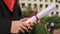 Close-up of female hands holding diploma with red ribbon, graduation ceremony