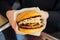 Close up female hands holding fast food beef burger on black background. American unhealthy calories meal. Selective focus, space