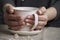 Close-up of female hands with a mug of beverage. Beautiful girl in grey clothes holding cup of tea or coffee