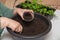 Close-up of female hands scoop compost into a pot for seedlings.