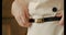 Close up of female hands touching the belt of a white dress on a white background wall, slow motion. fashionable trendy