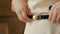 Close up of female hands touching the belt of a white dress on a white background wall, slow motion. fashionable trendy