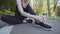 Close-up female legs of slender jogger runner woman in black sportwear sitting on track in park near water bottle after