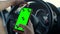 Close-up of a female phone hand with a green screen, the other hand on the steering wheel of a car. The girl driver