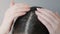 Close up of female's head. Woman dripping cosmetic oil on a hair parting and rubs it with fingers. Gray background