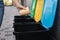 Close-up of female throwing cardboard cup in recycling bin. Different colour of recycling bins outdoors. Side view of