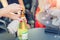 Close-up female waiter opening bottle of white champagne or prosecco at outdoor party on bright summer day. Girls hen-party