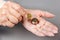 Close up of females wrinkled hands putting a euro coin in a stack of coins. Gray background. The concept of pension