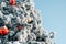 Close-up of festive snowy Christmas tree decorated with large toys balls against clear blue sky, outdoors. Merry christmas