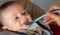 Close-up of a few months old baby starting weaning by eating a fruit puree