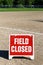 Close up of Field Closed sign on empty local baseball field, third base and baseline, on a sunny day with woods in the background