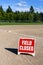 Close up of Field Closed sign on empty local baseball field, third base and baseline, on a sunny day with woods and blue sky in th