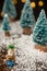 Close-up of figure of the Wise King Melchior with artificial Christmas trees on wooden table with snow, selective focus, with blac