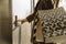 Close-up of a finger presses the elevator button. a woman with shopping bags in a beige raincoat calls the elevator