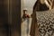 Close-up of a finger presses the elevator button. a woman with shopping bags in a beige raincoat calls the elevator