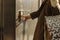 Close-up of a finger presses the elevator button. a woman with shopping bags in a beige raincoat calls the elevator