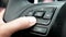 Close up of finger pressing the audio control buttons to increase or decrease the volume on the steering wheel when driving.
