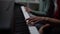 Close-up fingers of child boy playing piano, music teacher sits near and helps with playing during lesson.