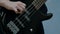 Close-up of the fingers of a teenager playing a black electric bass guitar. The guy pulled the strings on a musical