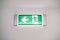 Close-up of a fire safety evacuation light sign with a running man and an arrow on the wall under the ceiling. Green